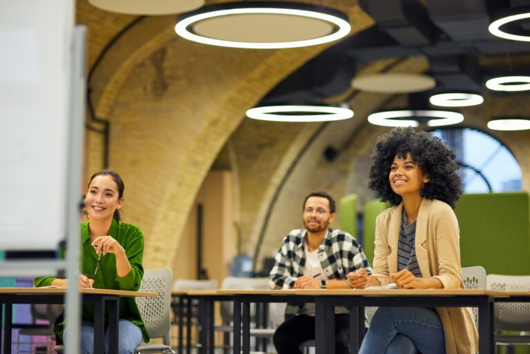 Group of young happy multiracial people sitting at desks in the modern office and listening to coach