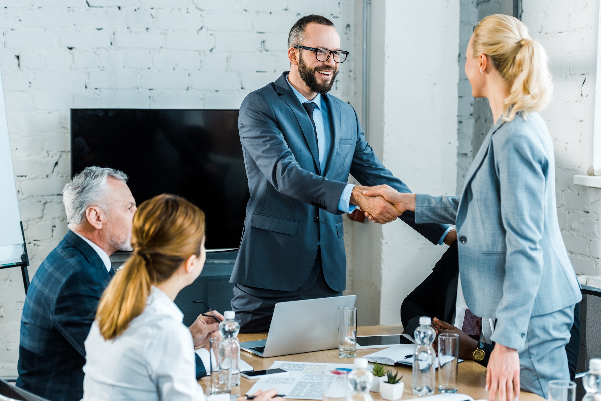 handsome business coach shaking hands with blonde woman near multicultural coworkers